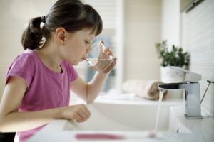 Little girl drinking water from faucet.