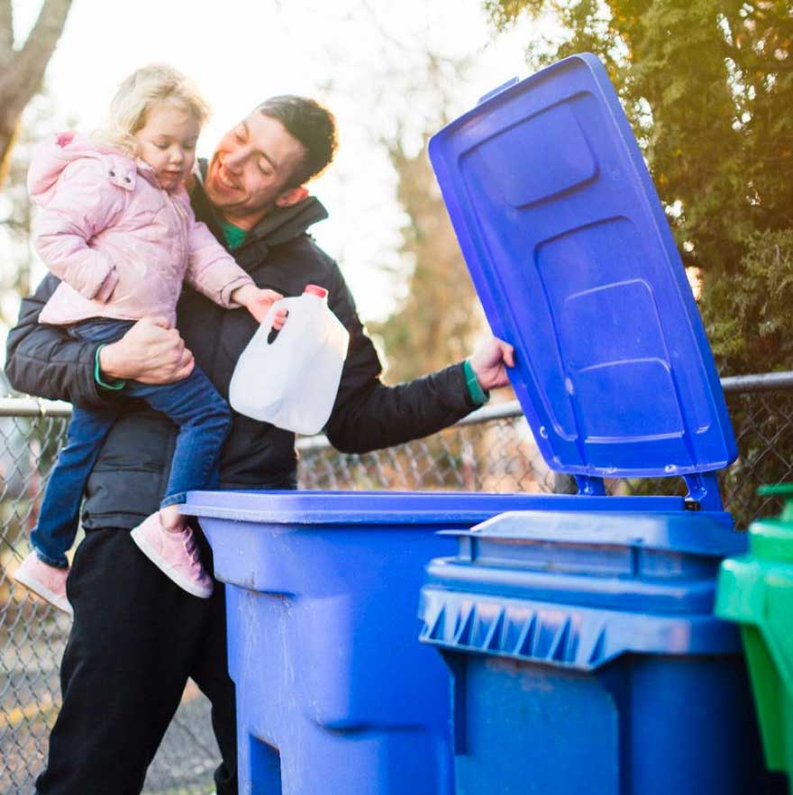 A father and his daughter recycle plastic in a bin.