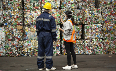 Male and female waste management workers standing in front of stacks of compacted recyclables.